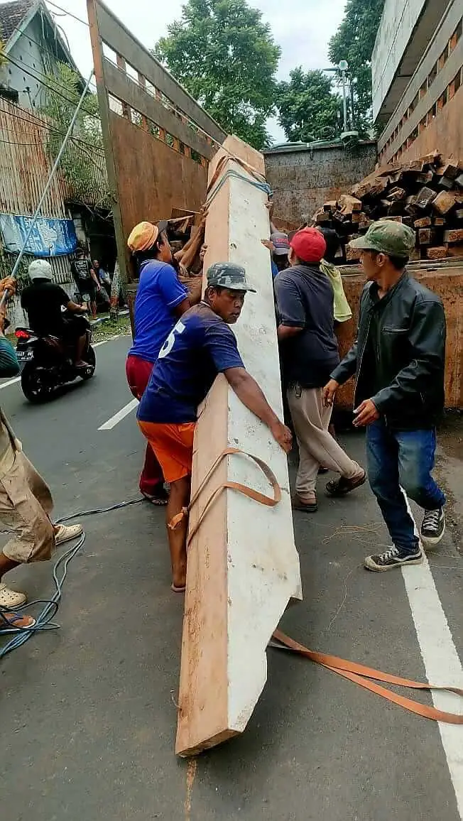 Workers carrying a long reclaimed teak beam towards a truck