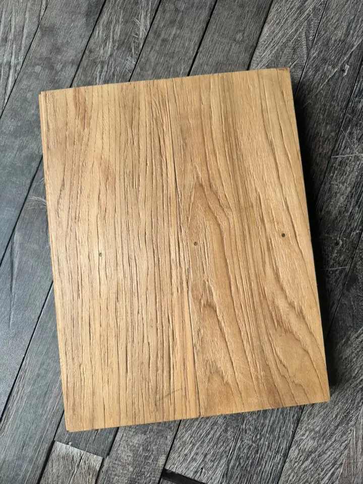 Teak flooring sample with a rustic, brushed surface in warm golden tones, on a grey wooden floor