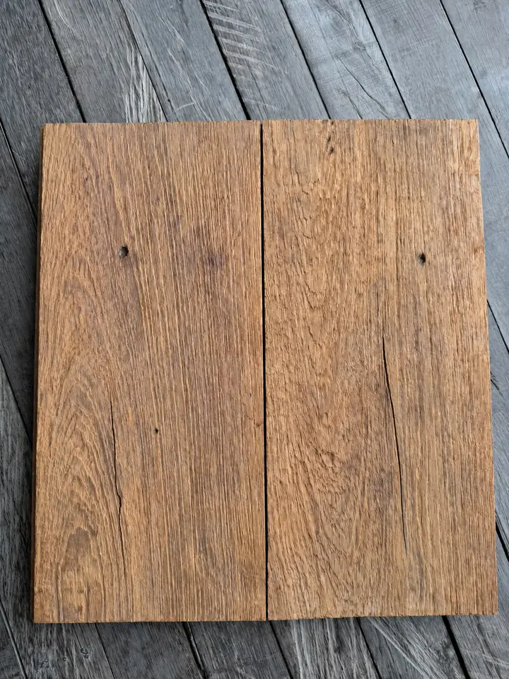Two rustic teak floorboards with old nail holes and cracks, laid on a grey wooden floor