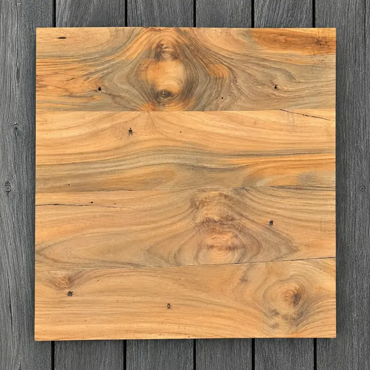 Four smooth teak floorboards laid side by side on a dark wooden floor, showing knots, small holes and colour variation