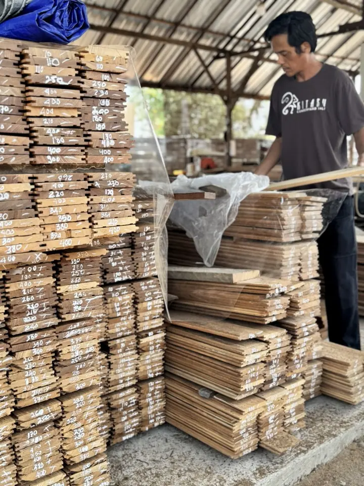 Stacks of teak flooring boards marked by hand in the Kitaru yard, with a team member preparing a pack