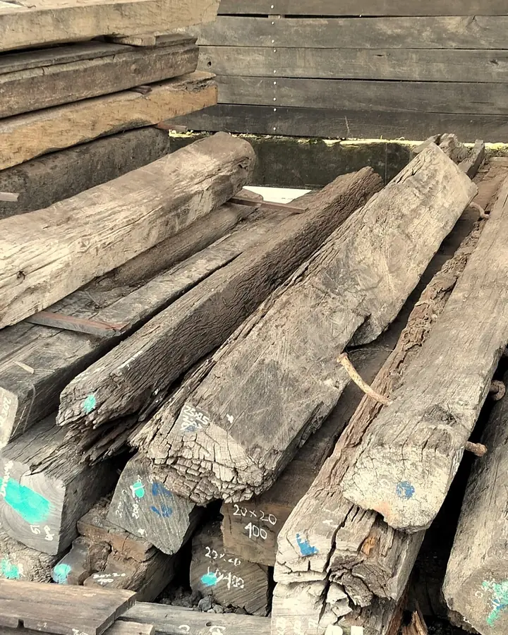 Reclaimed timber beams and planks stacked at the Kitaru lumberyard, marked with paint and labels
